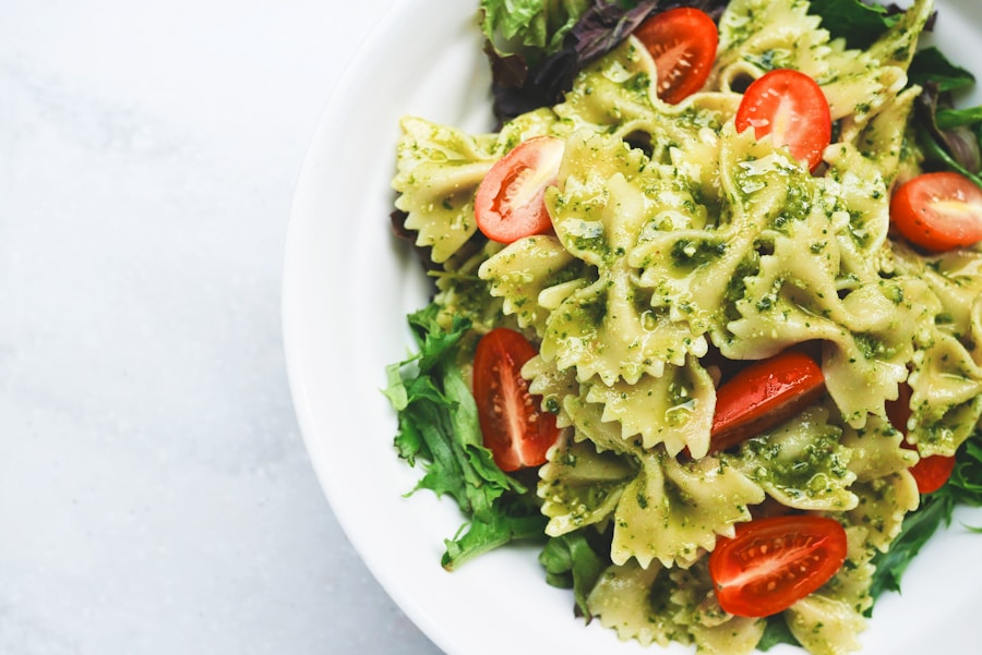 Farfalle pasta with green pesto, cherry tomatoes, and fresh greens on a white plate